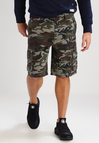 Vihreät ja ruskeat camo cargo-shortsit, joissa on useita taskuja ja rento leikkaus, yhdistettynä mustiin urheilukenkäiin. Pehmeä kangas.