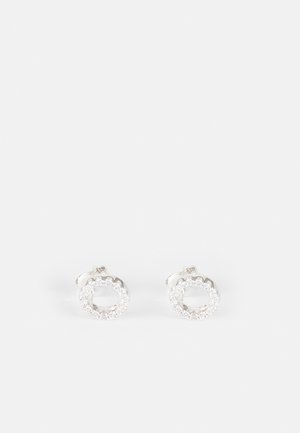 Paire de boucles d'oreilles clous en argent en forme de cercles ouverts avec de petites pierres précieuses claires serties tout autour des bords sur fond blanc.