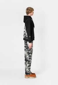 Sudadera negra con un patrón texturizado en gris y blanco, combinada con pantalones con un patrón en blanco y negro. Zapatos marrones con suelas claras.