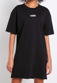 Czarna bawełniana sukienka t-shirt o luźnym kroju, z krótkimi rękawami i białym logo Vans na piersi. Gładka tekstura, bez wzorów.