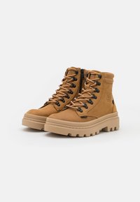 Bottes de randonnée en cuir tan, avec une tige haute, des œillets noirs, une semelle en caoutchouc striée et une fermeture éclair à l'avant pour un accès facile. Présente un logo sur le côté.