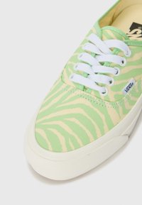 Green and yellow striped canvas sneaker with white laces, featuring a rubber sole and a small logo tag on the side.