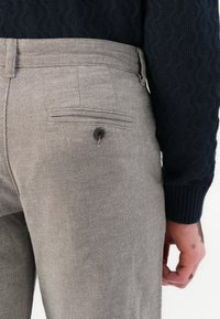 Gray patterned trousers with a textured fabric. Rear pocket features a button closure. A navy knitted sweater is partially visible.