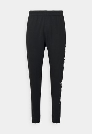 Černé joggingové kalhoty vyrobené z měkké tkaniny, s těsným střihem, elastickým pasem a bílým logem podél strany.