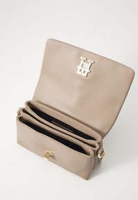 Beige nahkakäekott, millel on kuldne metallikinniti, ühes osas ja kaks sisepakki musta voodriga. Sile tekstuur.