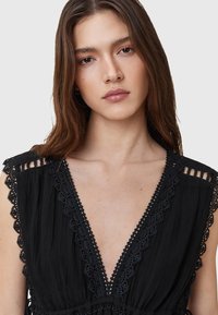 Vestito nero con profondo scollo a V, caratterizzato da dettagli in pizzo intricati lungo il collo e le spalle, e un tessuto testurizzato.