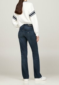 Vaqueros de mezclilla azul oscuro acampanados con cintura alta y bolsillos traseros, combinados con un suéter blanco con rayas marinas en las mangas.