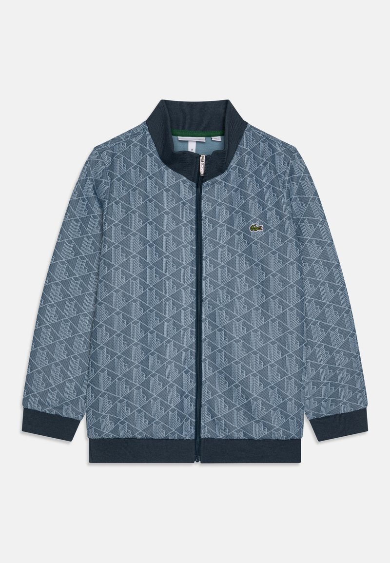 Zippered jacket in blue and navy, featuring an all-over geometric pattern. Ribbed collar and cuffs, with a small green logo accent.