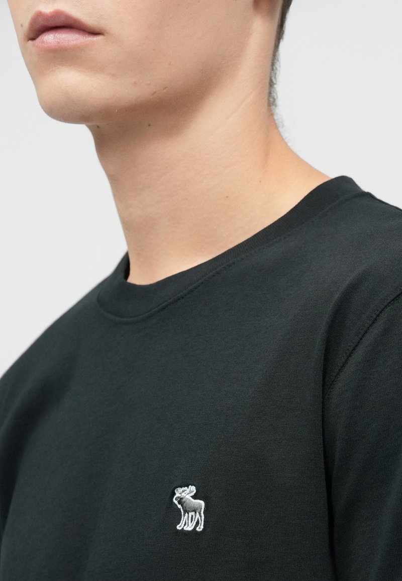 Sweat-shirt noir à manches courtes en coton. Présente un petit logo de orignal brodé sur le côté gauche de la poitrine. Texture lisse.