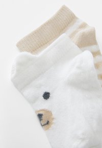 Katoenen sokken in een witte kleur met een berenontwerp, samen met beige gestreepte sokken, voorzien van een zachte geribbelde boord.