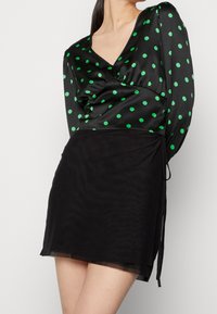 Abito nero con scollatura a V, con top in satin a pois verdi e gonna trasparente. Laccetti laterali per una vestibilità regolabile.