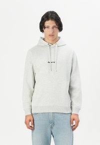 Felpa grigia in cotone con tasca frontale, cordini e testo nero sul petto. Abbinata a jeans azzurri chiari. Design semplice e casual.