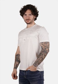 T-shirt bianco in cotone a maniche corte, con grafiche testurizzate in grigio chiaro e una vestibilità comoda. Il modello presenta un design minimalista.