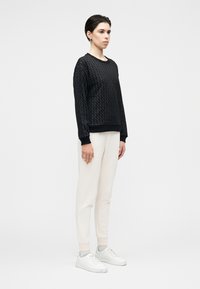 Sweatshirt preta texturizada, corte descontraído, punhos e bainha canelados. Combinada com calças de treino creme e ténis brancos, estilo minimalista.