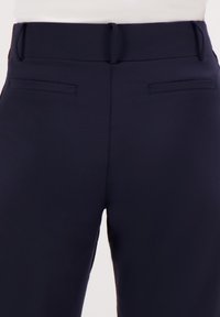 Navyblauwe high-waisted broek met een gladde textuur, voorzien van twee achterzakken en een verborgen sluiting bij de taille.