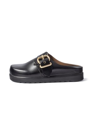 Zwarte leren instapslipper met dikke zool en grote gouden gesp aan de zijkant, getoond op een witte achtergrond.