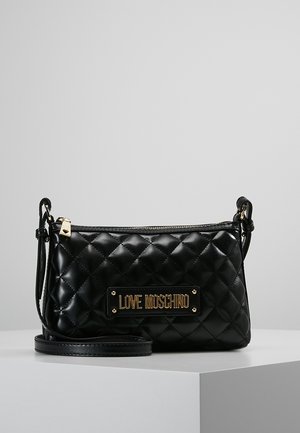 Schwarze gesteppte Leder-Umhängetasche mit goldener "LOVE MOSCHINO"-Logoplakette und Reißverschluss, präsentiert auf einem weißen Podest.