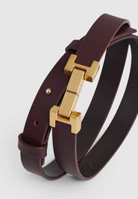 Burgundy színű bőr öv, arany színű fém csattal, geometrikus mintával. Az öv sima, látható varrással és állítható lyukakkal rendelkezik.