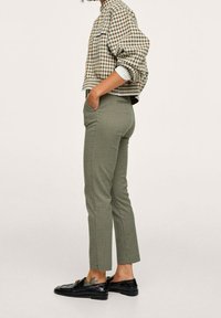 Chemise courte à carreaux marron et blanche, pantalon sur mesure vert olive avec un petit motif pied-de-poule, et mocassins noirs.