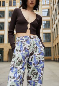 Sweater cropped castanho com detalhe em recorte circular, combinado com calças de moletão soltas com um padrão floral e abstrato colorido.