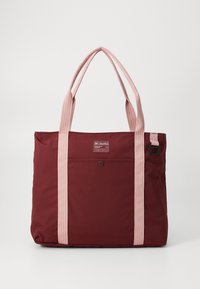 Mørkebrun totebag med lyserøde stropper i stof, der har en lomme på forsiden, et logo-patch og en blød tekstur. Lukkes med en lynlås øverst.