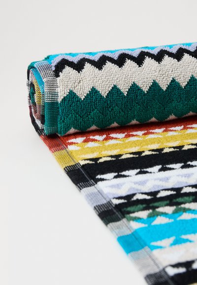 Flerfarget håndkle med zigzagmønster. Har striper i teal, svart, hvit og rød. Myk tekstur med løkkete stoff for absorbering.