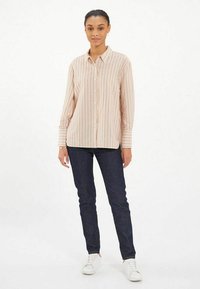 Chemise boutonnée rayée rose pâle à manches longues et détails de poignet, associée à un jean en denim foncé et des baskets blanches.