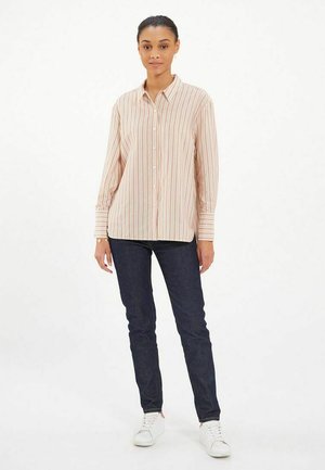 Chemise boutonnée rayée rose pâle à manches longues et détails de poignet, associée à un jean en denim foncé et des baskets blanches.