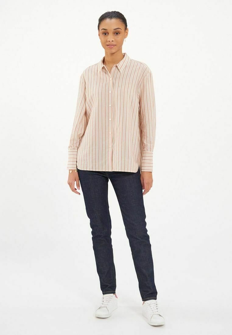 Chemise boutonnée rayée rose pâle à manches longues et détails de poignet, associée à un jean en denim foncé et des baskets blanches.