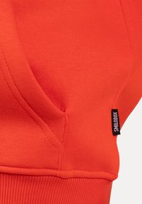 Rode, gestructureerde sweatshirtstof met een buidelzak. Heeft een geribbelde zoom en een klein zwart label met de tekst "SKILOODX."