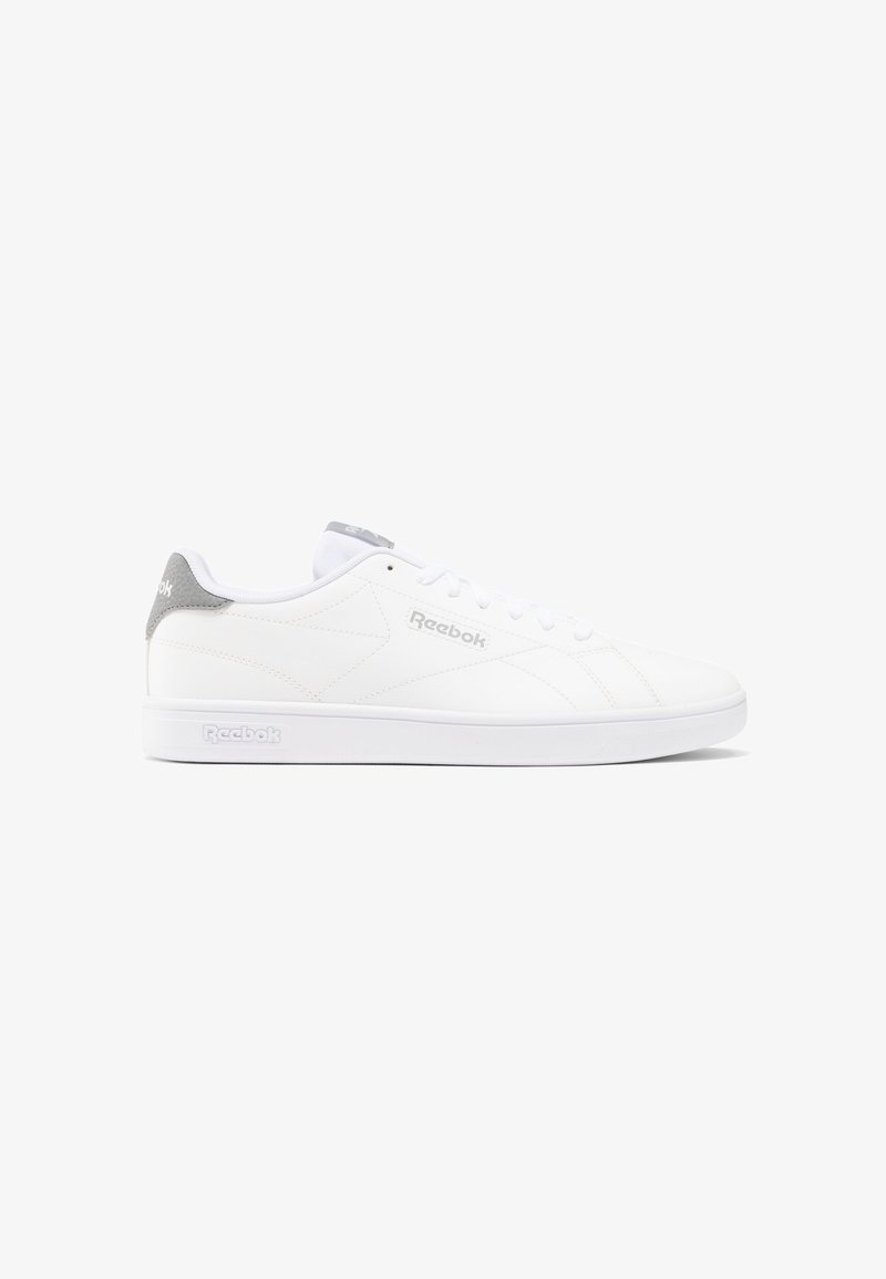 Zapatilla deportiva blanca con un upper de cuero liso. Presenta un acento gris en el talón y un diseño texturizado. Cierre con cordones.