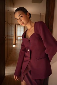 Burgundin väriä oleva räätälöity bleiseri, jossa on syvä kaula-aukko, kolme hopeista nappia ja pitkät hihat. Kangas on sileä ja hyvin muotoiltu.