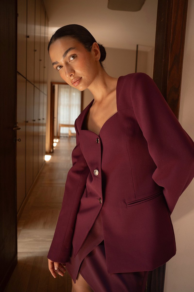 Burgundin väriä oleva räätälöity bleiseri, jossa on syvä kaula-aukko, kolme hopeista nappia ja pitkät hihat. Kangas on sileä ja hyvin muotoiltu.