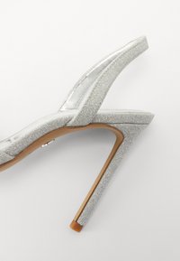Strieborné trblietavé sandále na vysokom podpätku s elegantným dizajnom, otvorenou špičkou a úzkym popruhom okolo členka. Podpätok je v štýle stiletto s textúrovaným povrchom.