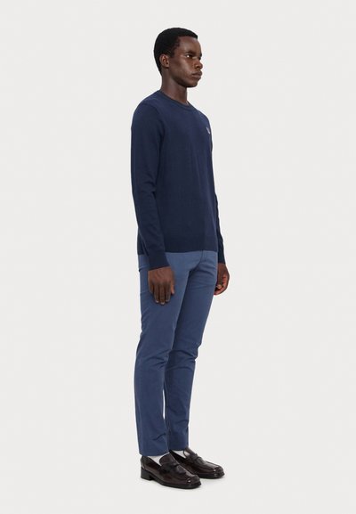 Navy knit sweater with long sleeves, paired with light blue trousers and black loafers. Simple design, smooth texture, no visible patterns.
