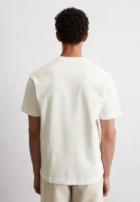 Light cream short-sleeve t-shirt made of soft fabric with a relaxed fit, featuring a rounded neckline and minimal stitching details.