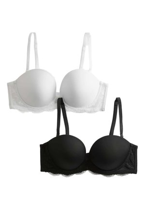 Donna che indossa un reggiseno imbottito nero con rifiniture in pizzo e mutandine nere in stile bikini abbinate, in piedi davanti a uno sfondo chiaro e uniforme.