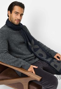 Marineblauer Schal mit grauer Schrift, aus weichem Stoff, über einem grauen Sweatshirt drapiert. Das Design zeichnet sich durch eine einfache und glatte Textur aus.
