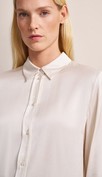 Pale beige blouse in smooth fabric, featuring a classic collar, button-down front, and long sleeves with a subtle sheen.