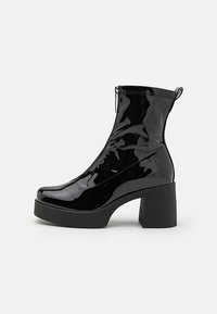 Botas de tobillo de charol negro con cremallera lateral, punta redondeada y un tacón grueso y texturizado. El diseño cuenta con un acabado suave y brillante.