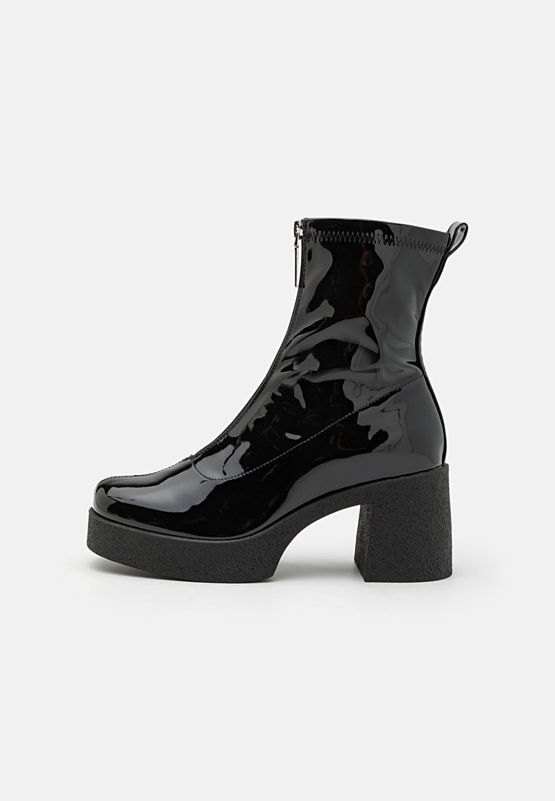 Botas de tobillo de charol negro con cremallera lateral, punta redondeada y un tacón grueso y texturizado. El diseño cuenta con un acabado suave y brillante.