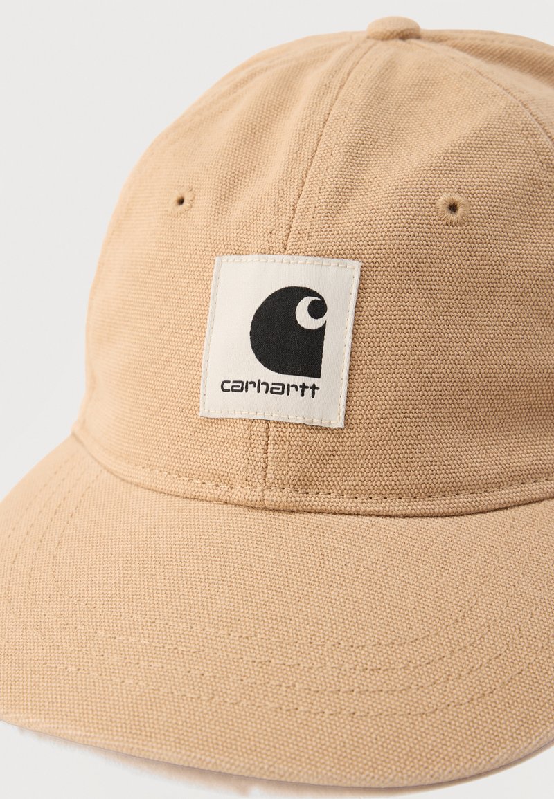 Beige Carhartt-Mütze mit aufgenähter Stofffläche und schwarzem Logo-Patch in der Mitte des Front-Panels.