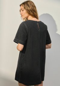 Schwarzes Denim-Kurzarmkleid mit lockerem Schnitt, das eine Rückenöffnung mit Knopfverschluss und Nahtdetails an den Ärmeln aufweist.