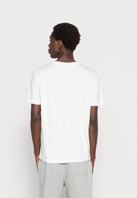 Camiseta de algodón blanca con cuello redondo y mangas cortas, que presenta un corte relajado y una textura suave. La vista trasera muestra un diseño minimalista.