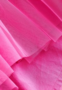 Rosa tyltyg med lager av genomskinlig textur, kombinerat med en solid rosa bas. Materialet är lätt och något skrynkligt.