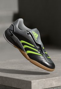Svart og grå sneaker med grønne detaljer, med et slankt design, teksturert overdel og gummisåle, som viser Adidas-logoen på en fremtredende måte.