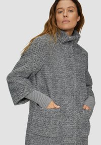 Manteau en tricot gris surdimensionné avec col montant, tissu texturé, épaules tombantes et poignets côtelés. Dispose de poches latérales pour plus de fonctionnalité.