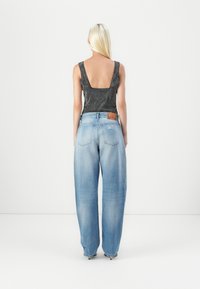 Black patterned sleeveless top with a low back, paired with light blue, wide-leg denim jeans featuring a distressed finish and label.