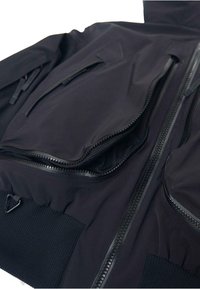 Fekete dzseki több cipzárral és hálós béléssel ellátott zsebekkel, bordázott mandzsettákkal és sima, vízálló anyagú textúrával.