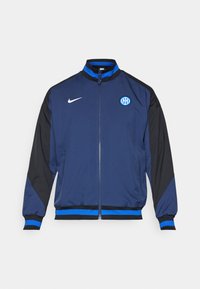 Giacca blu navy con maniche nere, dotata di zip completa, polsini a costine, dettagli blu e un logo circolare nella zona sinistra del petto.